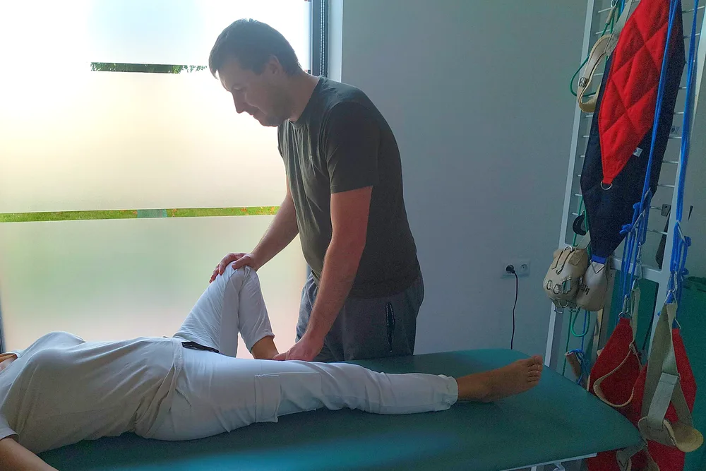 Łukasz Zgardziński bada staw kolanowy pacjentki leżącej na stole